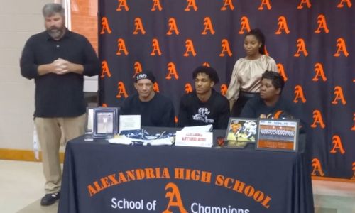 Alexandria’s Antonio Ross dons an Alabama cap and shirt as Alexandria coach Todd Ginn (left) and family members look on during Wednesday’s signing-day ceremony in Larry R. Ginn Gymnssium.