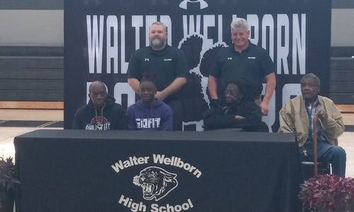 Wellborn wrestler Ahmad Noel sits with grandparents Frankie and Ralph Noel, Jr., and father Alfred Noel plus Wellborn wrestling coach Ben Carroll (standing, left) and Wellborn football coach Jeff Smith during Tuesday’s ceremony in the school’s gymnasium. (Photo by Joe Medley)
