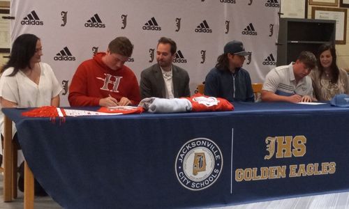 Jacksonville High’s Hayden Smith (left) and Zach Limberis sign Wednesday as family members look on in the school’s library. Smith will play ESports for Huntingdon College, and Limberis will play golf for Point University. (Photo by Joe Medley/EASportsToday.com)