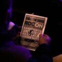 An audience member reviews the program for ROC ON, a concert event featuring Randy Owen, Jamey Johnson, Riley Green, and Gordon Mote, held at Jacksonville State University.