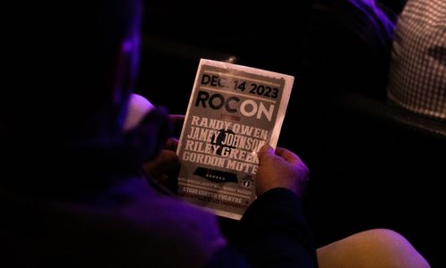 An audience member reviews the program for ROC ON, a concert event featuring Randy Owen, Jamey Johnson, Riley Green, and Gordon Mote, held at Jacksonville State University.