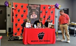 Weaver’s Brandon Jolliff puts pen to paper Wednesday as Weaver coach Andy Fulmer watches in the school library. (Photo by Joe Medley/East Alabama Sports Today)